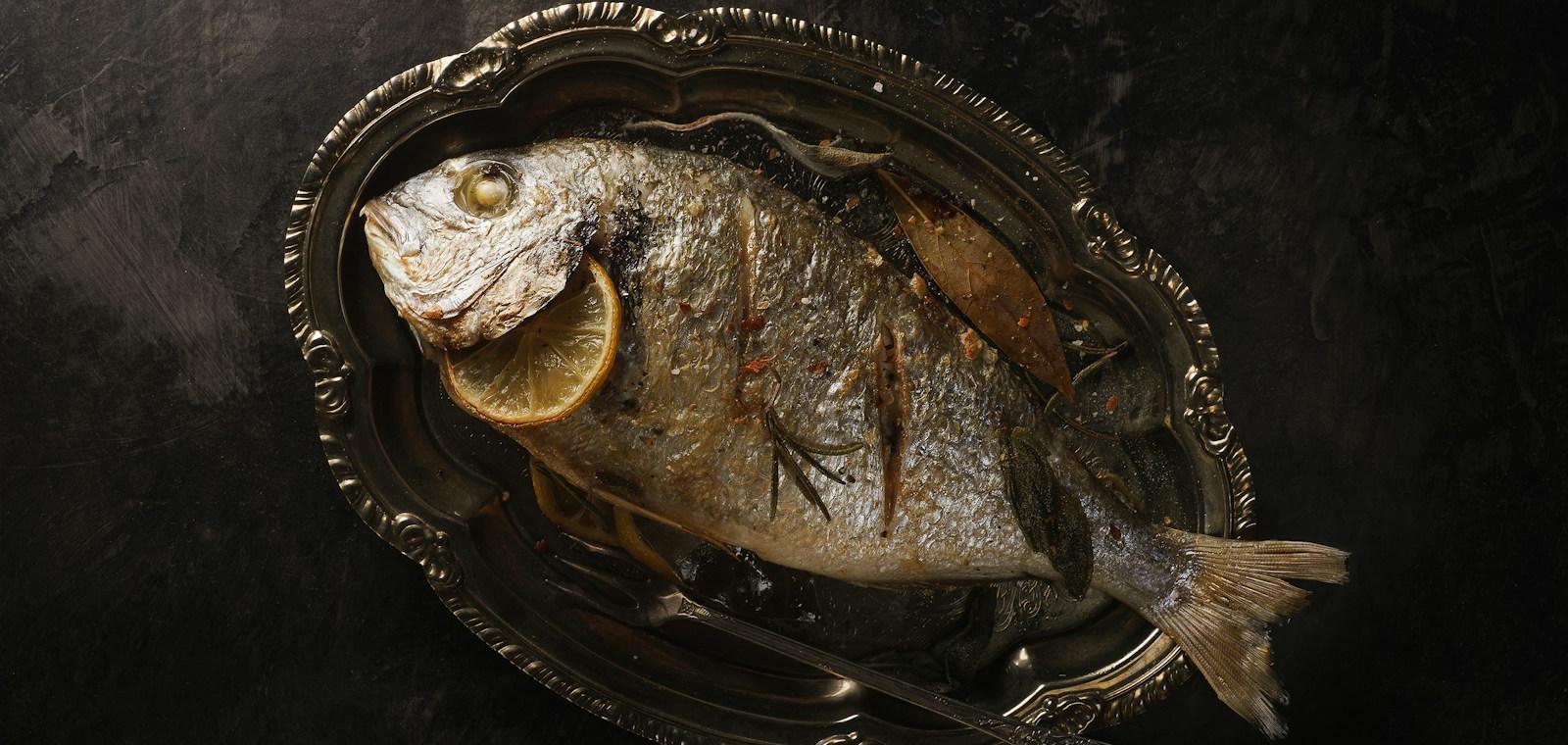A whole grilled sea bass with lemon on an antique silver platter