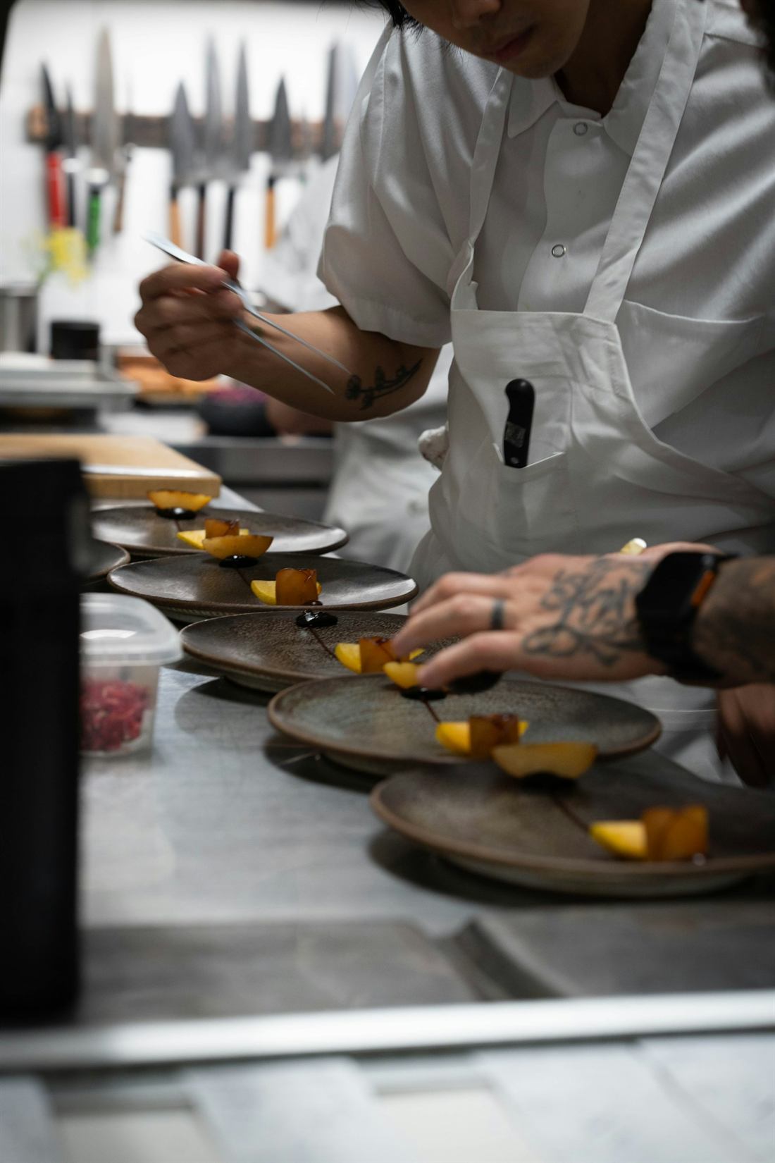 A chef in whites plating dishes along the pass in the kitchen