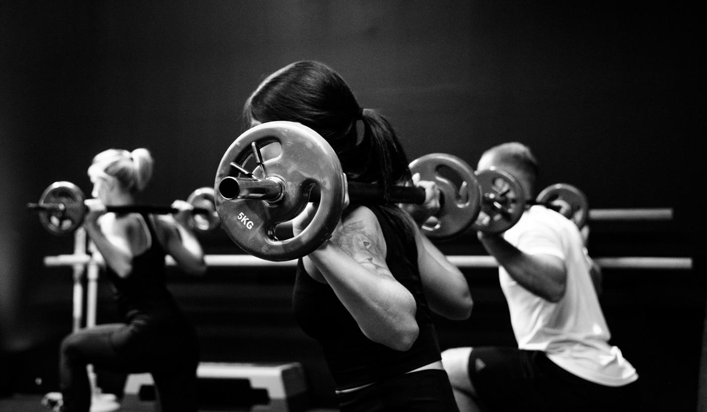 Three athletes in a row with barbells on their backs in a black and white gym