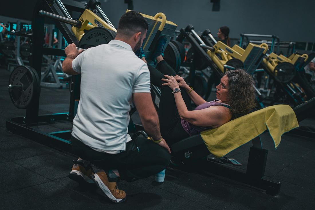 A coach crouching beside a member on a leg press, adjusting their position