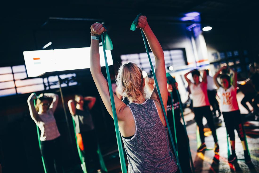 A group class in a dark gym pulling resistance bands overhead together