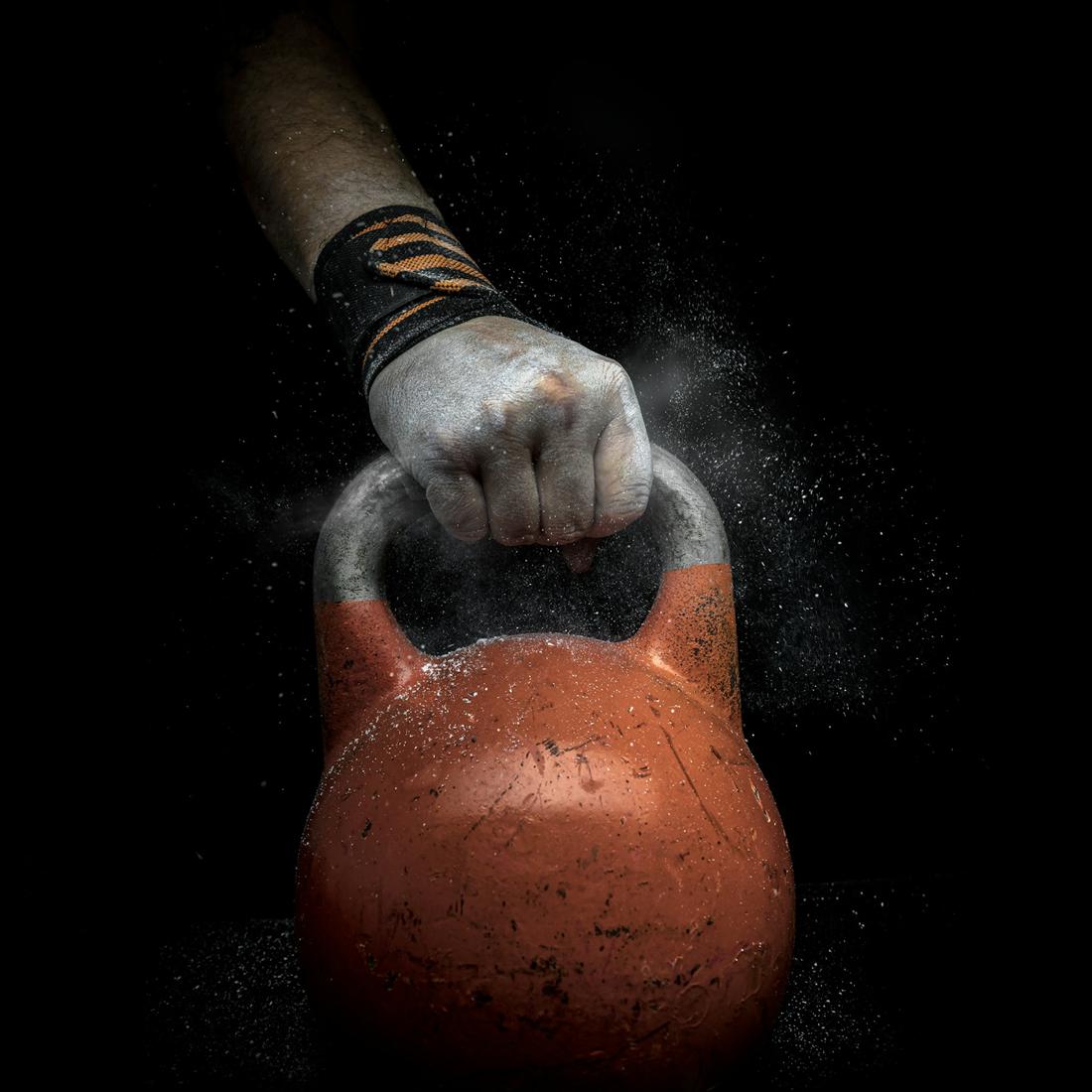 A chalked hand gripping a kettlebell, dust hanging in dark air