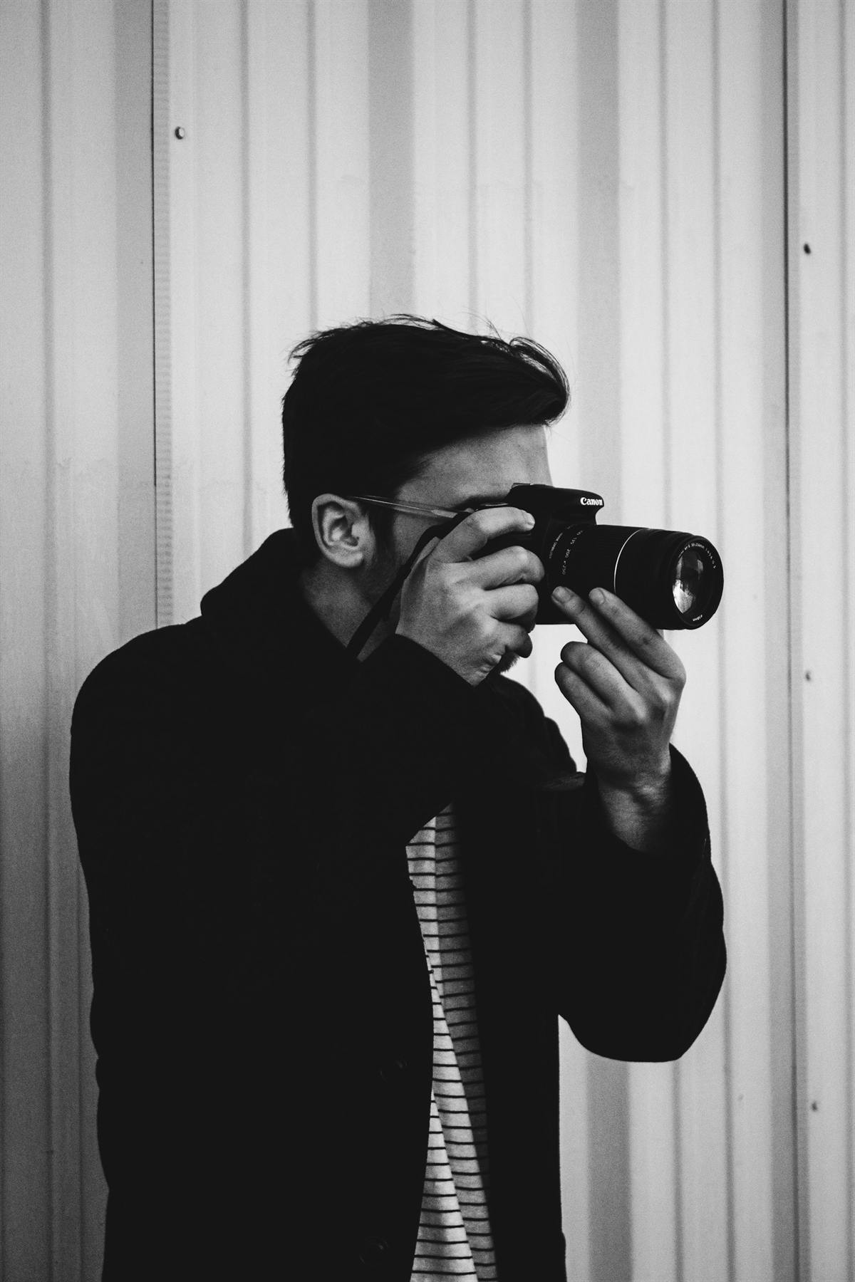 A photographer raising a camera to their eye against a corrugated wall