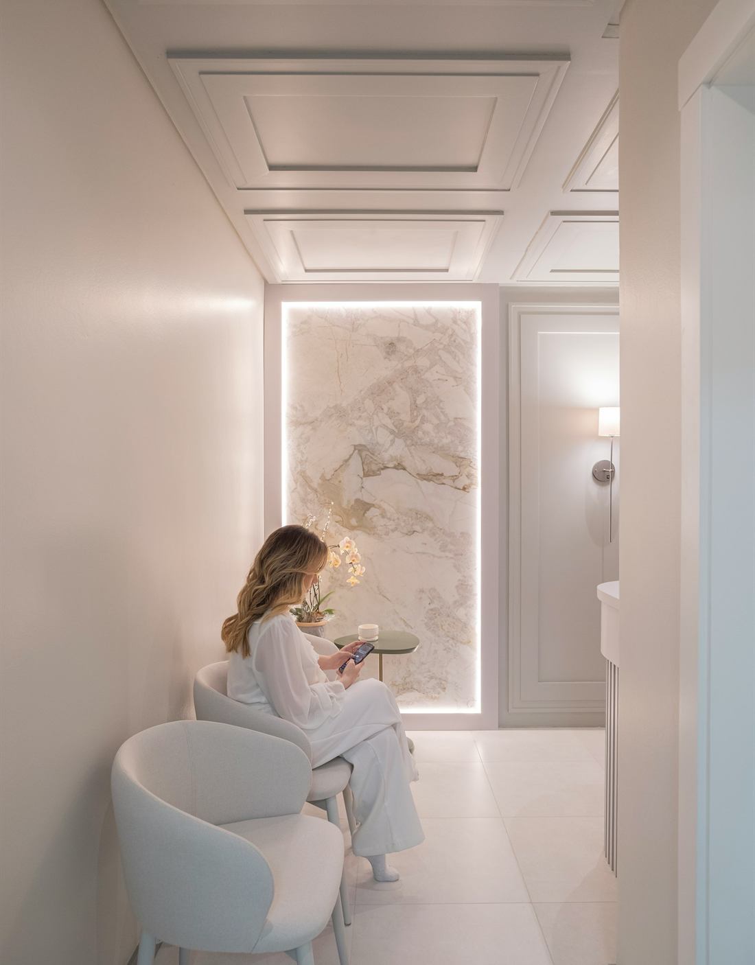 A woman in white sitting in a calm, softly lit waiting area with marble panelling