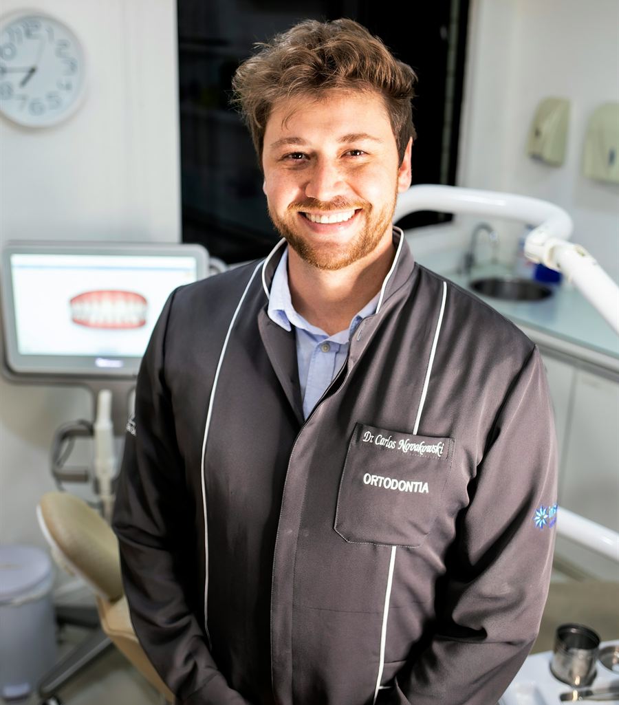 Portrait of Dr Ethan Marais, orthodontist, smiling in a dark clinic jacket beside a monitor