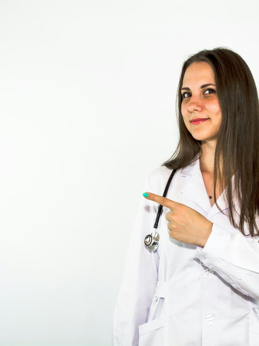 Portrait of Dr Naledi Khumalo in a white coat, pointing to one side and smiling