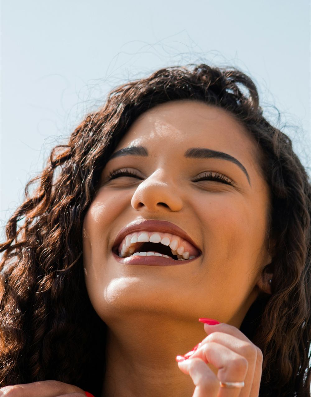 A woman with dark curly hair laughing and smiling upwards