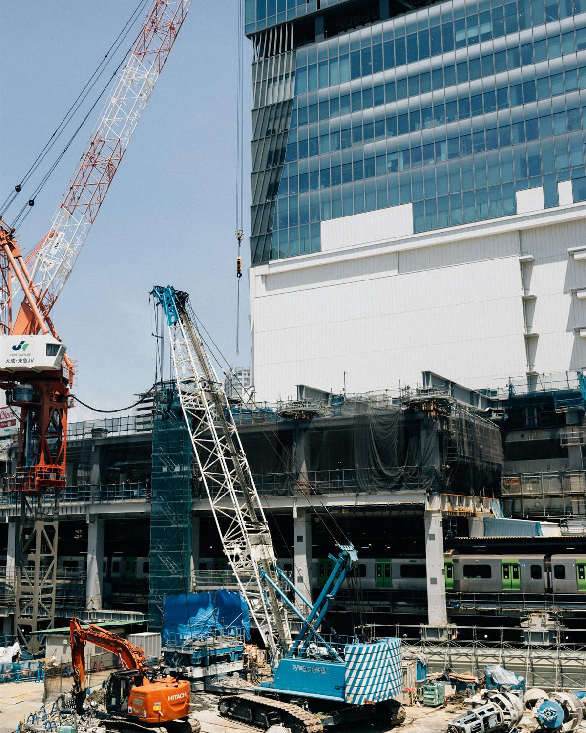 A busy construction site with cranes, excavators and a glass tower rising behind it