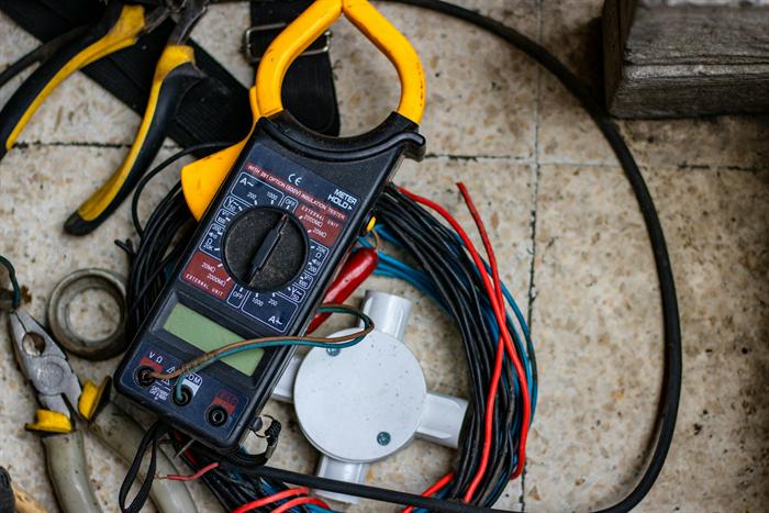 A clamp meter, pliers and cable on a tiled floor: testing equipment for electrical certification