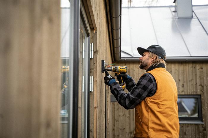 An electrician drilling a fixing for an outdoor electrical point on a timber wall